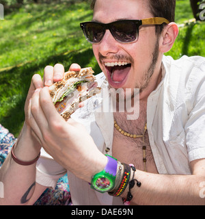 Uomo che indossa gli occhiali da sole di mangiare panino Foto Stock