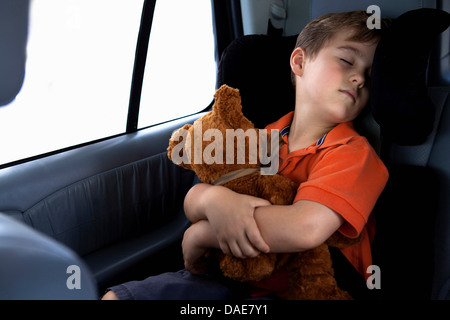 Ragazzo addormentato nel seggiolino di sicurezza in auto azienda orsacchiotto Foto Stock