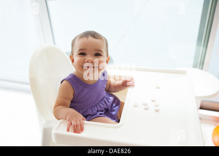 Baby girl seduto nella sedia alta sorridente, ritratto Foto Stock