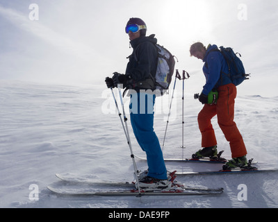 Due maschio sciatori sulle vacanze sciistiche backlit contro il sole sulle piste di neve nelle Alpi francesi nei pressi di Samoens, Rhone-Alpes, Francia, Europa Foto Stock