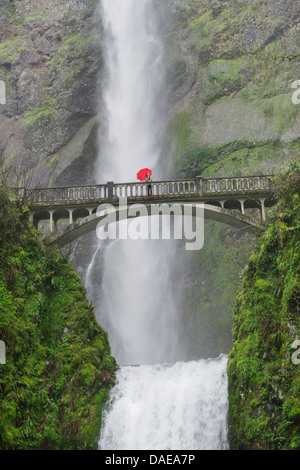 Donna con ombrello rosso su passerella su cascate Multnomah, Columbia River Gorge, STATI UNITI D'AMERICA Foto Stock