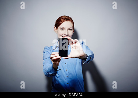 Studio Ritratto di giovane donna mantenendo la fotocamera del telefono Foto Stock