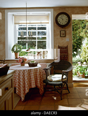 Orologio circolare sulla parete accanto a porta aperta nel cottage cucina con nero sedia di vimini accanto a tavola con panno controllati Foto Stock