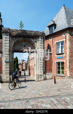 Ciclista cavalcando attraverso la porta principale di accesso del Grand Béguinage / Grande beghinaggio / Groot begijnhof, Leuven / Louvain, Belgio Foto Stock