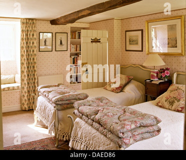 Ripiegate piumini sui letti gemelli con rose-cuscini modellato in cottage camera da letto con carta da parati rosa Foto Stock