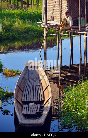 Uomo seduto sulla veranda della sua casa su una delle isole di nuoto sul Lago Inle, Birmania Foto Stock