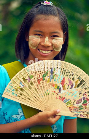 Ritratto di una giovane ragazza con ventola fatta con il tradizionale thanaka birmano, una protezione solare realizzato in pasta del thanaka tree, Birmania, Mandalay Foto Stock