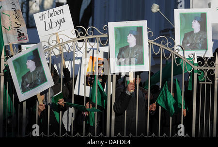 I sostenitori del sovrano libico Muammar Gheddafi cartelloni di onda portante una immagine del leader libico a manifestanti che hanno inscenato una protesta al di fuori dell'Ambasciata libica a Berlino, Germania, 21 febbraio 2011. I rapporti che indicano una diffusa e drammatica perdita di vita a proteste contro il governo in Libia si moltiplicano. Foto: Hannibal Hanschke Foto Stock