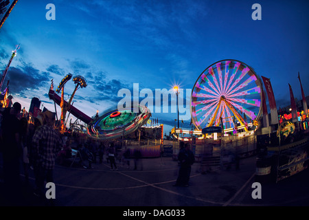 Calgary Stampede Amusement Rides; ruota panoramica Ferris e corse di filatura con luci accese al tramonto, appena dopo il tramonto. Foto Stock