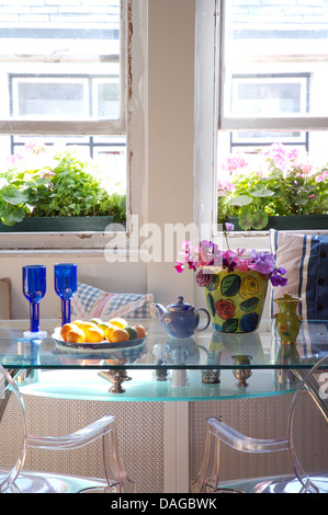 Sala da pranzo con gli occhiali blu e vaso di piselli dolci sul ripiano in vetro tavolo con coppia di Philippe Starck 'fantasma' sedie Foto Stock