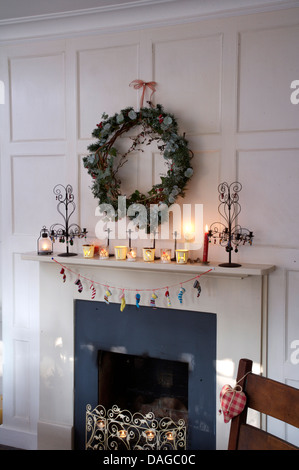 Edera e ghirlanda di conifere sopra il camino in bianco pannellata sala da pranzo decorato per il Natale con le candele accese sul mantelpiece Foto Stock