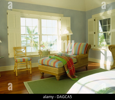 Coloratissimi cuscini a strisce sulla chaise longue nella parte anteriore del vetro bianco con persiane in stile piantagione in blu pallido Bermudan camera da letto Foto Stock