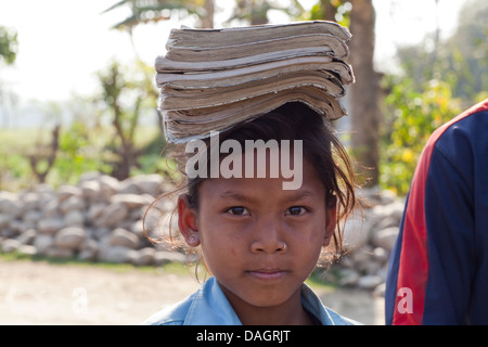 Scuola di Tharu ragazza portando la sua ben utilizzati libri bilanciato sulla sua testa. Bardia. Zona di Bheri, Regione Mid-Western, Terai. Il Nepal. Foto Stock