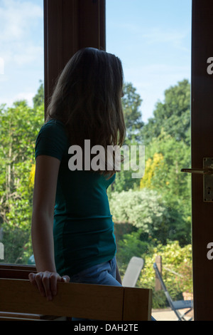 Ragazza in piedi nel buio da solo da una porta, fuori è un cielo azzurro e sole splendente nel giardino. Foto Stock