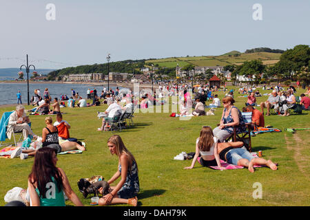 Largs, Nord Ayrshire, Scozia, Regno Unito, Sabato, 13 luglio, 2013. Persone che siedono sull'erba accanto al Firth di Clyde godendo il caldo tempo soleggiato Foto Stock