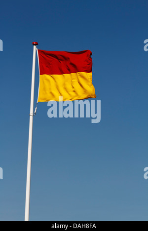 Il bagnino di segnalazione di bandiera lifeguard pattugliato la zona di balneazione, contro un cielo blu, Kastrup Beach, Copenhagen, Danimarca Foto Stock