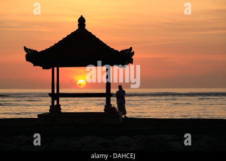 Una persona in piedi accanto a una pagoda balinesi sulla spiaggia di Sanur, Bali. Prese a sunrise. Bali, Indonesia Foto Stock