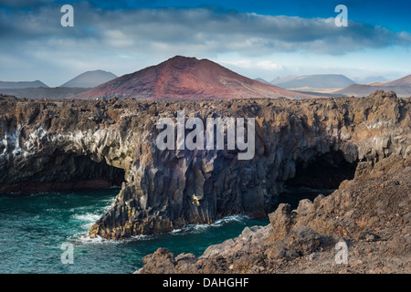 Grotte marine erose in flussi storici di lava aa a Los Hervideros, Lanzarote, Isole Canarie, con Montana Bermeja e altri coni giovani sullo sfondo Foto Stock