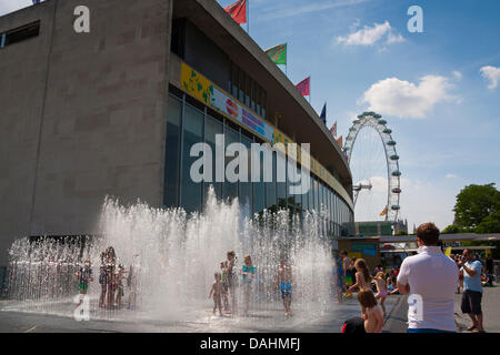 Londra, Regno Unito. 14 Luglio, 2013. Bambini, guardato da erede ai genitori di godere l'acqua fredda di una fontana al centro di Southbank, come temperature Volate in alto venti nel centro di Londra. Credito: Paolo Davey/Alamy Live News Foto Stock