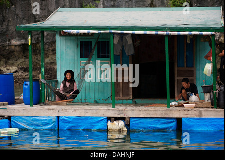 Il vietnamita casa galleggiante con la donna in amaca e uomo di mangiare, Halong Bay, Vietnam Foto Stock