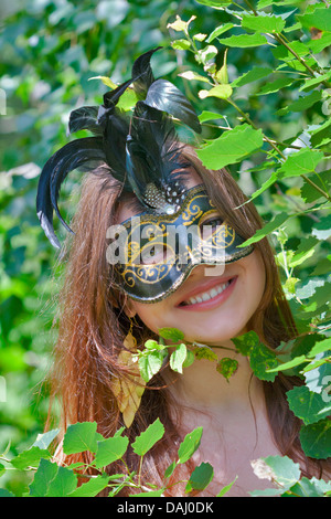 Giovani abbastanza occhi verdi che pongono la donna in estate foresta con carnevale veneziano mask Foto Stock