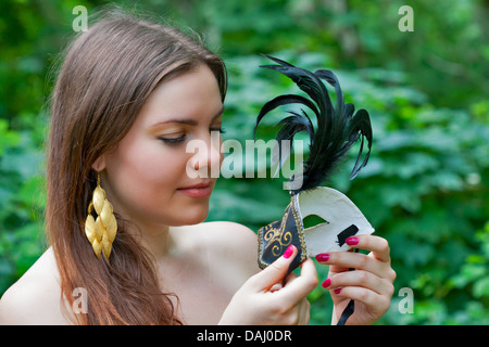 Piuttosto giovane donna che guarda sul carnevale veneziano maschera nella foresta Foto Stock