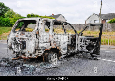 Newtownabbey, Irlanda del Nord. 15 Luglio 2013 - Un bruciato auto blocca una strada principale dopo i tumulti a Newtownabbey Foto Stock