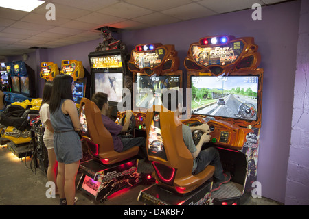 Teens ottenere una scarica di adrenalina al video arcade guida auto da corsa ad alta velocità a Coney Island, Foto Stock