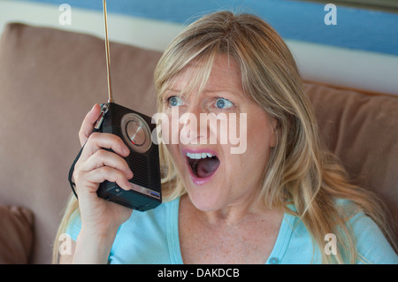 Donna bionda con sguardo scioccato sulla sua faccia ascoltando la radio a transistor. Foto Stock