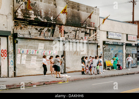 Multietniche locali attendere per un autobus di fronte a fuoco negozi danneggiati in South Central Los Angeles dopo il 1992 Rodney King sommossa. Foto Stock