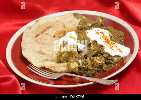 Saag pollo al curry, servita con pane piatto e yogurt cosparso con peperoncino rosso. Foto Stock