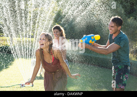 Amici a giocare con le pistole di acqua in impianti sprinkler in cortile Foto Stock