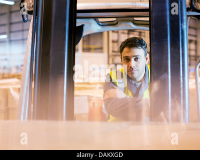 Lavoratore operante il carrello elevatore in magazzino Foto Stock