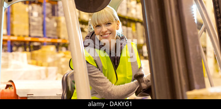 Lavoratore operante il carrello elevatore in magazzino Foto Stock