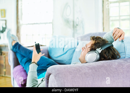 Uomo che ascolta le cuffie sul divano Foto Stock