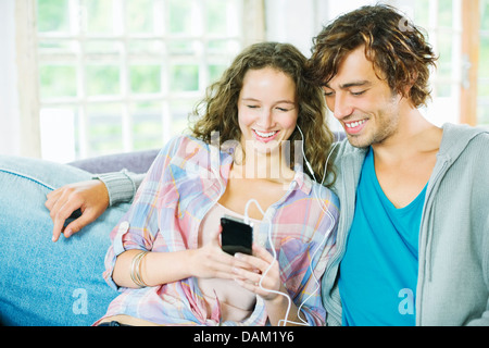 Paio di ascolto di auricolari insieme sul divano Foto Stock