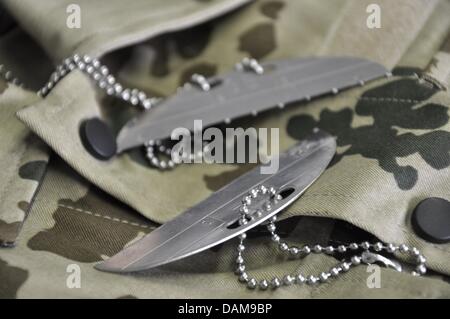 Rotto il tedesco Forze Armate dog tag giacciono su un campo uniforme in Berlino, Germania, 28 maggio 2011. Le dog tag, che ogni soldato deve indossare intorno al collo, contengono una codifica con i più importanti dati personali, incluso il personale Numero e nazionalità, e servire come una esatta identificazione del soldato, ad esempio in caso di morte, in cui la metà del tag rimane con il Foto Stock