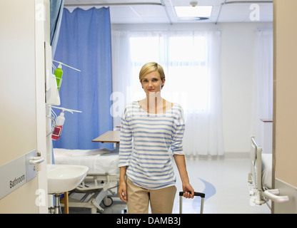 Paziente wheeling bagagli fuori della stanza di ospedale Foto Stock