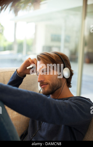 Uomo che ascolta le cuffie sul divano Foto Stock