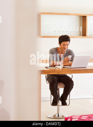 L'uomo mediante telefono cellulare e computer portatile a tavola Foto Stock