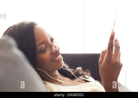 Donna in ascolto delle cuffie sul divano Foto Stock