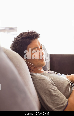 Uomo che ascolta le cuffie sul divano Foto Stock