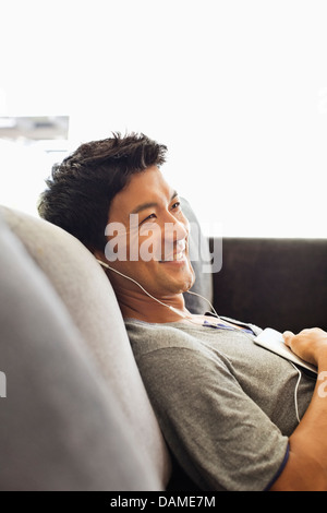 Uomo che ascolta le cuffie sul divano Foto Stock