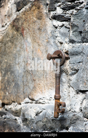 Vecchia chiave arrugginita appesi a un chiodo arrugginito in un muro di pietra Foto Stock