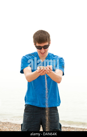 Un giovane uomo in piedi su una spiaggia e lasciando la sabbia corrono attraverso le sue dita Foto Stock