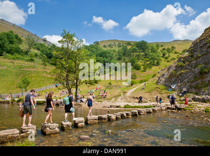 Turisti attraversando il fiume Colomba su pietre miliari nel Derbyshire Dovedale parco nazionale di Peak District Inghilterra UK GB EU Europe Foto Stock