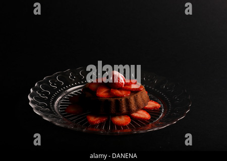 Limone vaniglia mini pan di spagna con fragola sulla parte superiore e le fragole tagliate sulla lastra di vetro e uno sfondo scuro Foto Stock