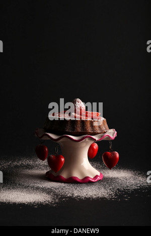 Il cioccolato pan di spagna con fragole e fette di fragola sulla sommità e zucchero a velo su antic stand con cuori rossi e di ghiaccio Foto Stock