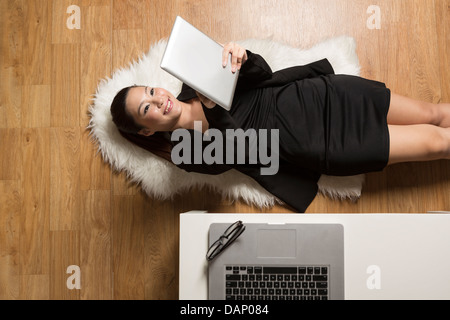 Giovane donna cinese giacente sul piano di lettura di un touch screen computer tablet Foto Stock