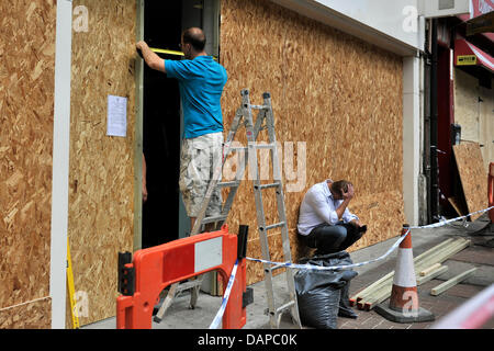 Un uomo copre le finestre di un negozio con doghe in legno mentre il suo collega è seduto sul terreno dopo i tumulti a Clapham, Londra, Gran Bretagna, 10 agosto 2011. Scontri e saccheggi hanno continuato a Londra e in molte altre città britanniche per la quarta notte in una fila. Foto: MARIUS BECKER Foto Stock